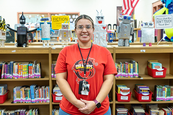 A woman in a red t-shirt smiles in front of bookshelves