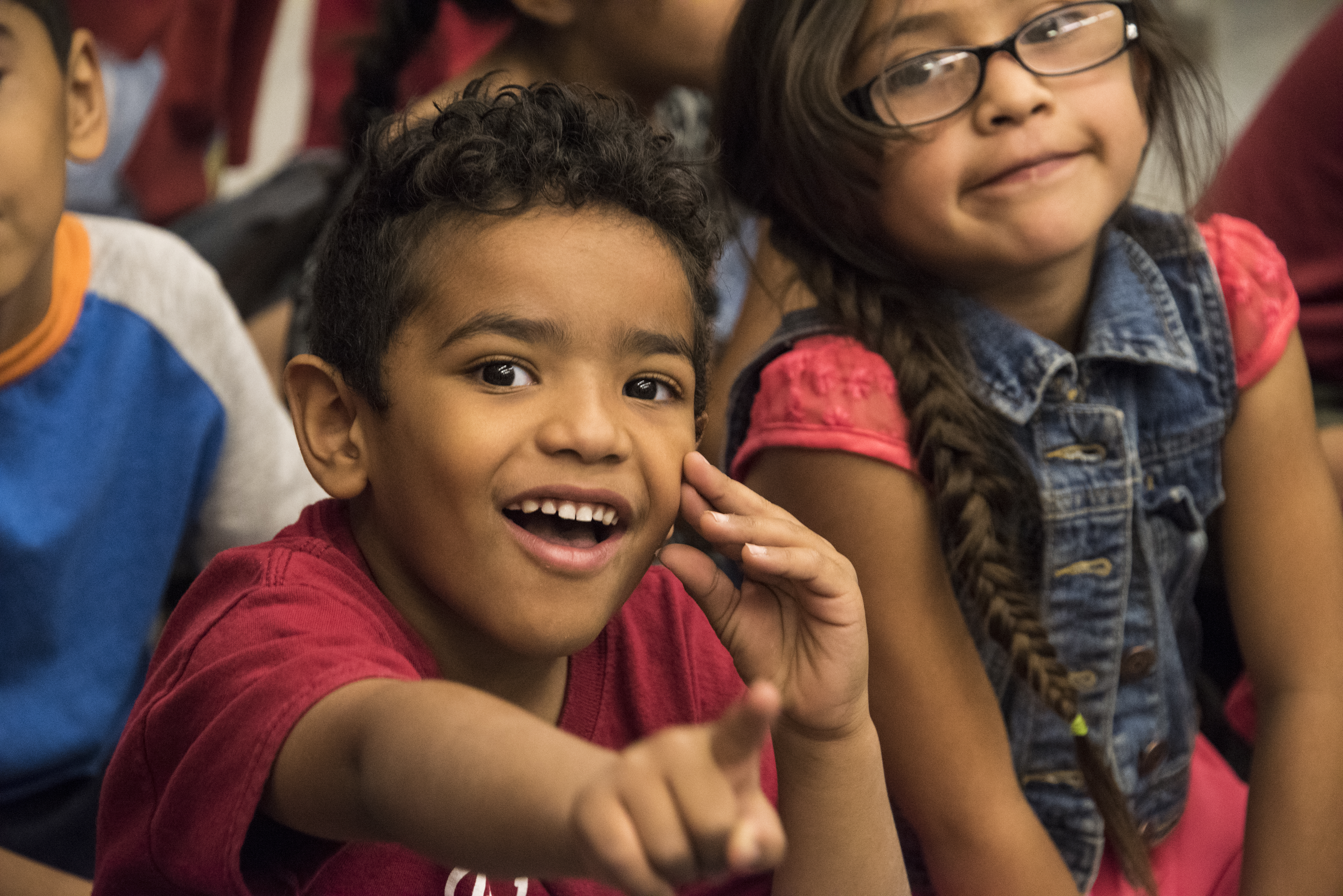 A little boy smiles and points to something during an assembly